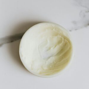 Creamy skincare product in round container on marble surface.