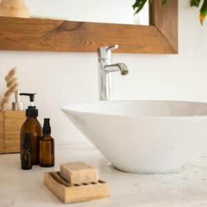 Interior of bathroom table with soap and cosmetic oil placed near white sink and faucet under mirror in wooden frame in modern apartment