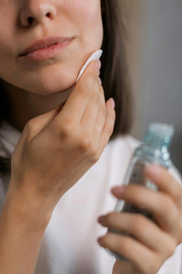 Close-up of a woman applying skincare product to her face with a cotton pad, showcasing beauty care routine.