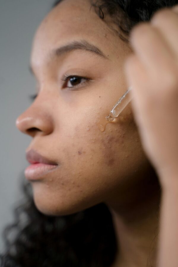 Close-up side view of a woman applying serum to her skin in a studio setting.